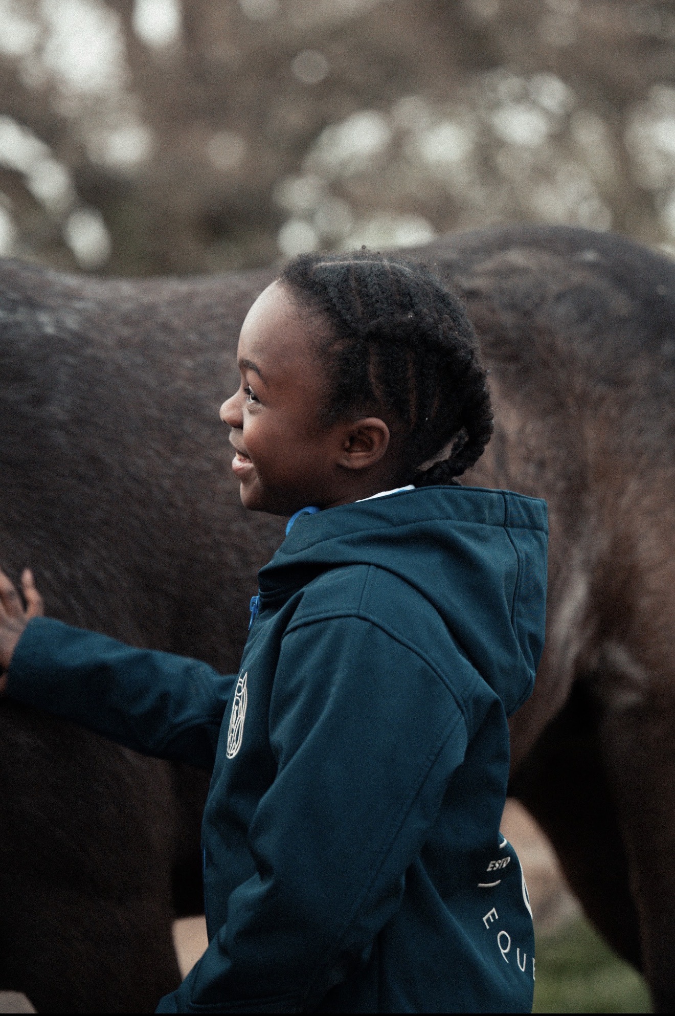 Young rider smiling beside a horse in a navy Champion Pride jacket
