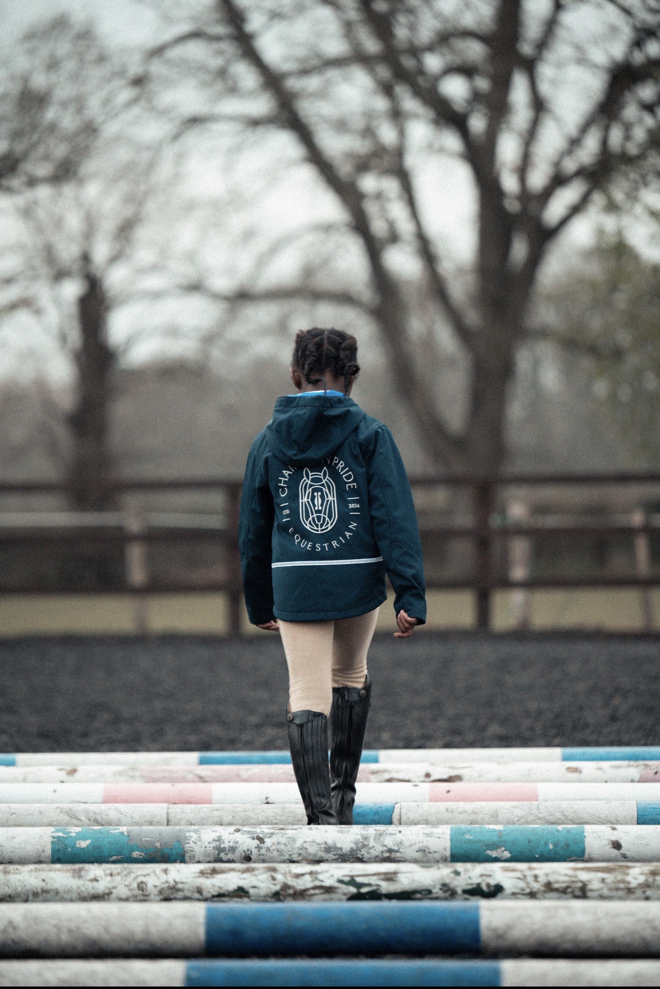 Young rider walking over ground poles, seen from behind in a navy Champion Pride jacket